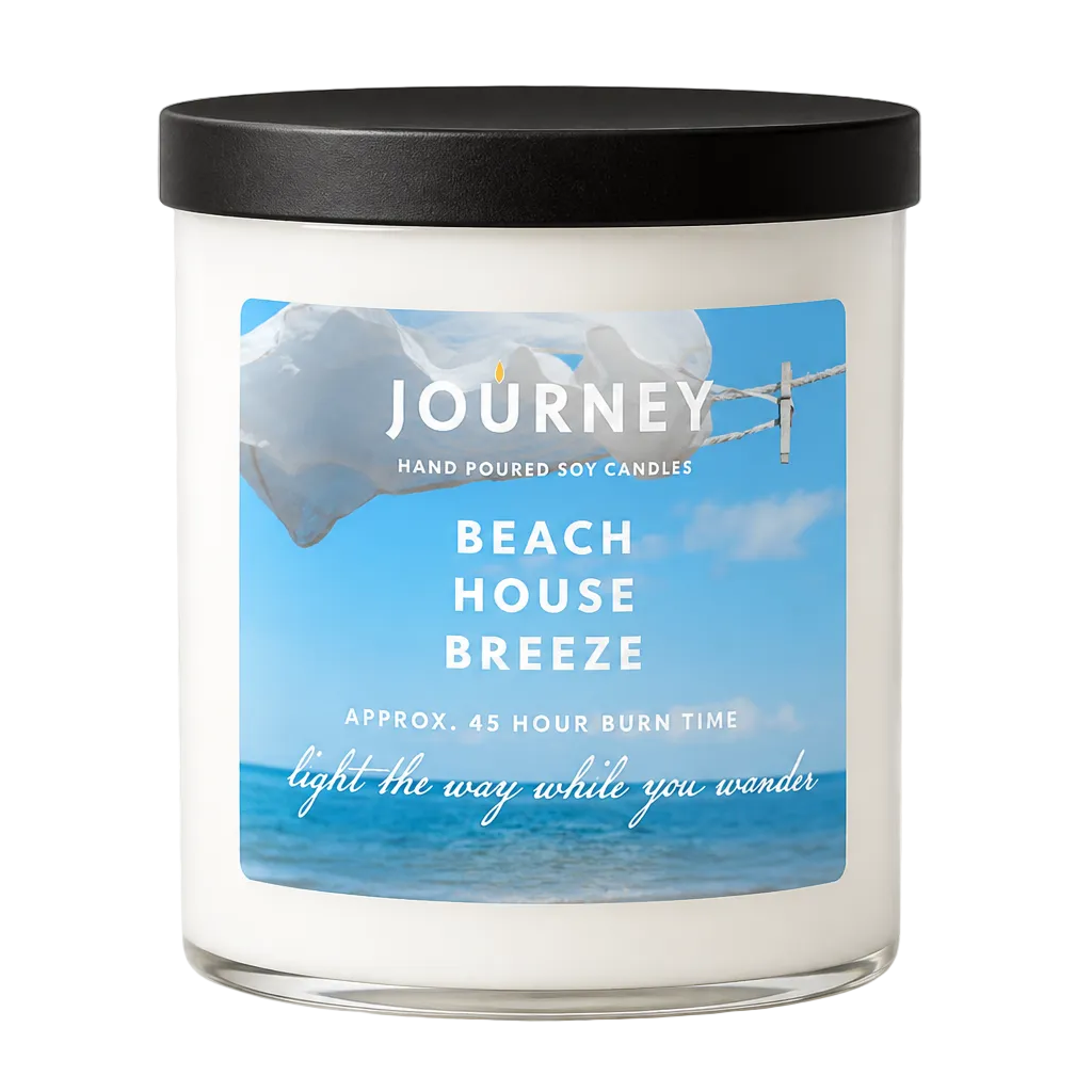 Candle in a white glass jar with matte black lid. Label shows Journey brand mark and the fragrance Beach House Breeze.