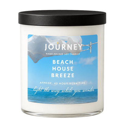 Candle in a white glass jar with matte black lid. Label shows Journey brand mark and the fragrance Beach House Breeze.