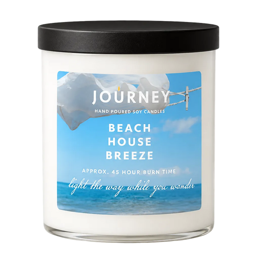 Candle in a white glass jar with matte black lid. Label shows Journey brand mark and the fragrance Beach House Breeze.